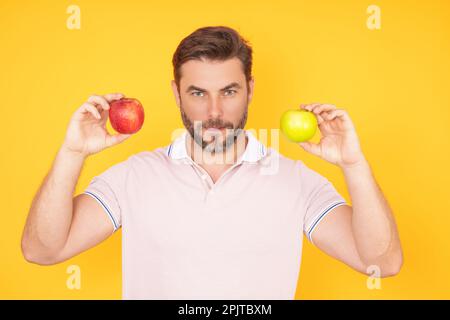 Ein Mann, der leckeren Apfel bastelt. Mann isst Apfel, Studioporträt. Frühstück am Morgen. Mann mit gesunden Zähnen, der Äpfel auf gelb isoliertem Hintergrund hält Stockfoto