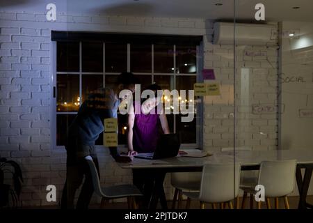 Verschiedene Geschäftsleute stehen am Schreibtisch, verwenden Laptops und diskutieren, arbeiten bis spät in die Nacht im Büro Stockfoto