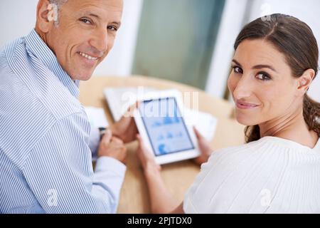 Wir lieben diese Zahlen. Porträt von zwei Kollegen, die zusammen an einem Schreibtisch sitzen und in ihrem Büro ein digitales Tablet verwenden. Stockfoto