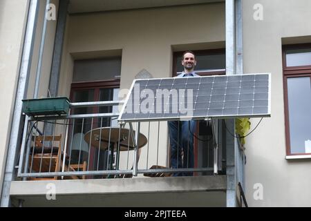 Leipzig, Deutschland. 30. März 2023. Ein Mann steht auf dem Balkon seiner Wohnung hinter einem Solarmodul, das von der Leipziger Firma Priwatt hergestellt wurde. Das Unternehmen stellt sogenannte Balkonkraftwerke für Wohnungen her. (Zu dpa: 'Boom in Solarsystemen - das Mini-Kraftwerk für den Balkon') Kredit: Sebastian Willnow/dpa/Alamy Live News Stockfoto