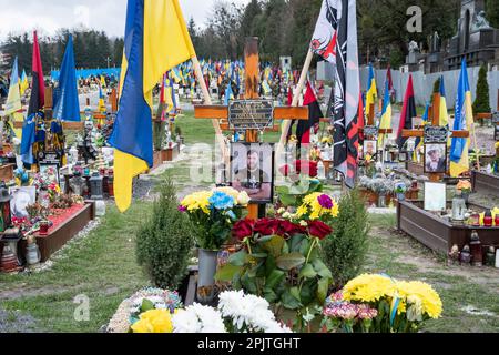 Das Grab eines gefallenen Soldaten mit einem Porträt auf dem Ehrenfeld auf dem Friedhof in Lemberg. Yurii Ruf war Schriftsteller, öffentliche Figur, Patriot der Ukraine und eine bekannte Person in Lemberg und der Ukraine. Er organisierte viele Veranstaltungen, ein Festival usw. Als der Krieg begann, ging er als Freiwilliger an die Front und wurde bei einer Kampfmission in der Region Luhansk am 1. April 2022 getötet. Das Ereignis auf den Fotos ist das Gedenken an Jurij in der Kirche und auf dem Feld der ehrenvollen Beerdigungen auf dem Friedhof Lychakivskyi in Lemberg am ersten Jahrestag seines Todes. Verwandte, Freunde und Bewohner von Stockfoto