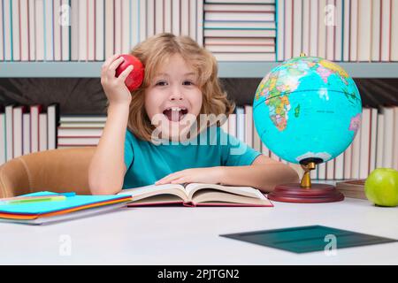 Schuljunge mit Büchern und Apfel in der Bibliothek. Kleines Schülerkind. Porträt eines Nerdschülers mit Schulbedarf. Stockfoto