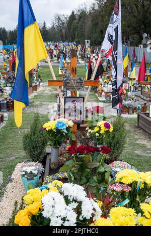 Das Grab eines gefallenen Soldaten mit einem Porträt auf dem Ehrenfeld auf dem Friedhof in Lemberg. Yurii Ruf war Schriftsteller, öffentliche Figur, Patriot der Ukraine und eine bekannte Person in Lemberg und der Ukraine. Er organisierte viele Veranstaltungen, ein Festival usw. Als der Krieg begann, ging er als Freiwilliger an die Front und wurde bei einer Kampfmission in der Region Luhansk am 1. April 2022 getötet. Das Ereignis auf den Fotos ist das Gedenken an Jurij in der Kirche und auf dem Feld der ehrenvollen Beerdigungen auf dem Friedhof Lychakivskyi in Lemberg am ersten Jahrestag seines Todes. Verwandte, Freunde und Bewohner von Stockfoto