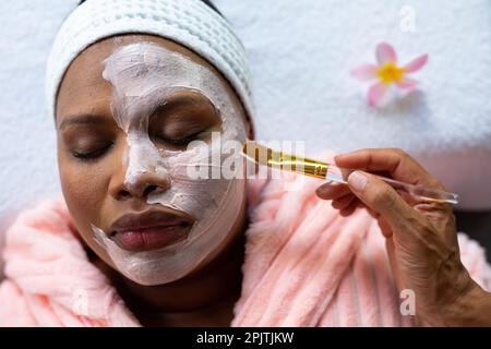 Entspannte, große afroamerikanische Frau mit Beauty-Gesichtsmaske auf Gesicht im Spa Stockfoto