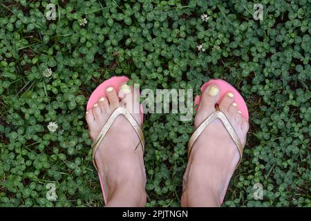 Frau mit stilvollen Flip-Flops auf grünem Gras im Freien, Draufsicht Stockfoto