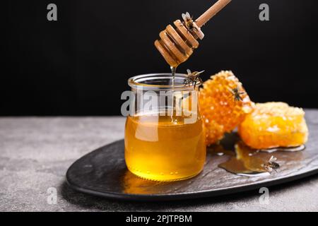 Leckerer frischer Honig und Bienen auf grauem Tisch Stockfoto
