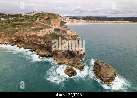Luftaufnahme eines Leuchtturms auf einer Klippe mit einer Festung in der Stadt Nazare, Portugal Stockfoto