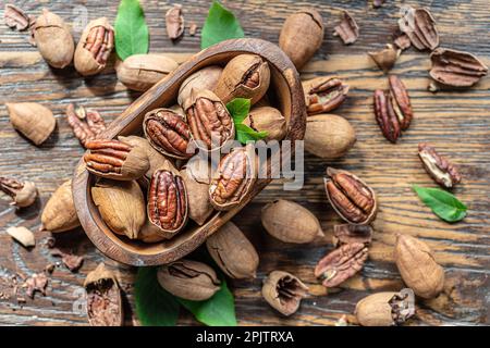 Geschälte und rissige Pekannüsse in der Holzschale auf dem Holztisch. Draufsicht. Stockfoto