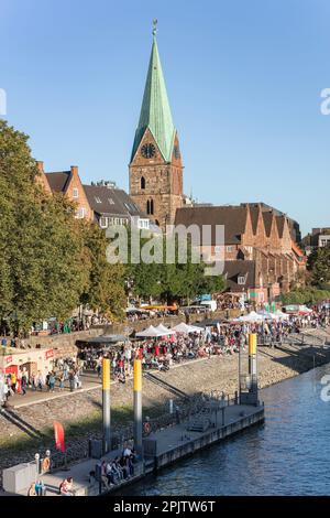 Die Menschen feiern den Martime Day - Maritime Woche in Cafés und Bars an der historischen Schlachte Uferpromenade an der Weser bei der St. Martin's Church. Bremen. Stockfoto