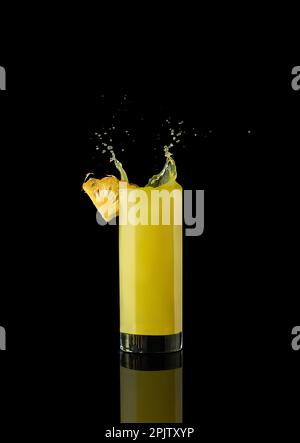 Ananassaft in einem Glas auf schwarzem Hintergrund mit Reflexionen und Spritzwasser. Hochwertiges Foto Stockfoto