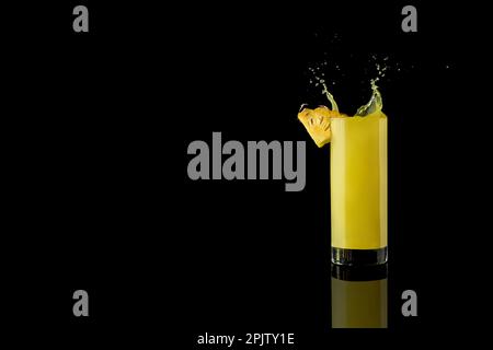 Ananassaft in einem Glas auf schwarzem Hintergrund mit Reflexionen und Spritzwasser. Hochwertiges Foto Stockfoto