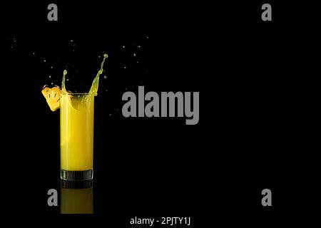 Ananassaft in einem Glas auf schwarzem Hintergrund mit Reflexionen und Spritzwasser. Hochwertiges Foto Stockfoto