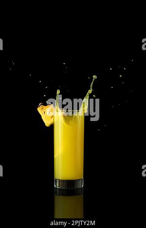 Ananassaft in einem Glas auf schwarzem Hintergrund mit Reflexionen und Spritzwasser. Hochwertiges Foto Stockfoto