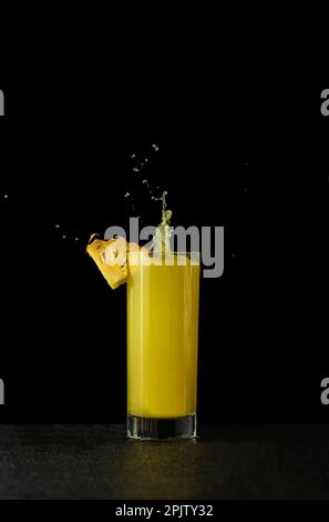 Ananassaft in einem Glas auf schwarzem Hintergrund mit Reflexionen und Spritzwasser. Hochwertiges Foto Stockfoto