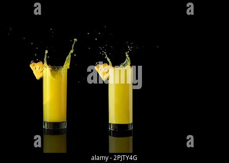 Ananassaft in einem Glas auf schwarzem Hintergrund mit Reflexionen und Spritzwasser. Hochwertiges Foto Stockfoto