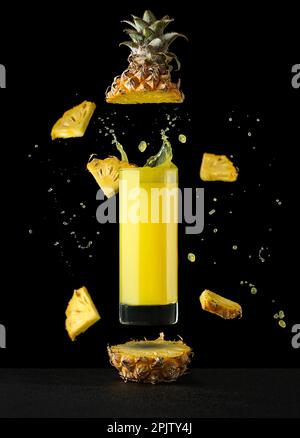 Ananassaft in einem Glas auf schwarzem Hintergrund mit Reflexionen und Spritzwasser. Hochwertiges Foto Stockfoto