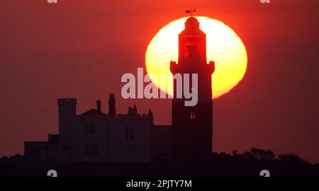 Die Sonne geht hinter dem Leuchtturm von Coquet Island auf, der sich 1,2 km vor der Küste von Northumberland in der Nähe von Amble befindet und zu einem Haufen voller Aktivitäten mit bis zu 35.000 Seevögeln auf der Insel wird. Foto: Dienstag, 4. April 2023. Stockfoto