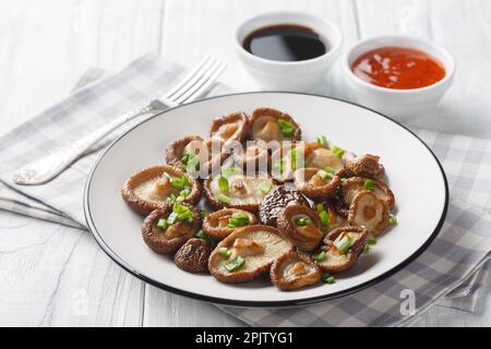 Gebratene Shiitake-Pilze mit grünen Zwiebeln und scharfen Saucen auf einem Holztisch. Horizontal Stockfoto