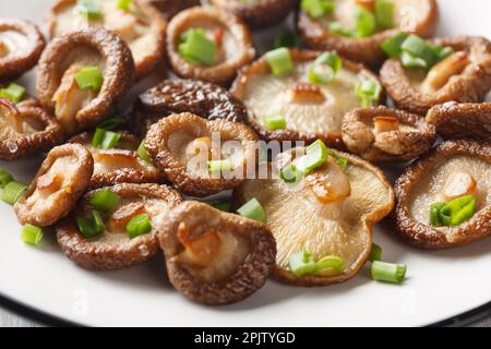 Hausgemachte, frisch gebratene Shiitake-Pilze mit grünen Zwiebeln, Nahaufnahme auf einem weißen Teller. Horizontal Stockfoto