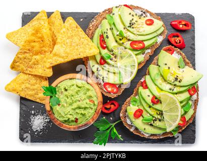 Avocado-Toasts, Guacamole und Tortilla-Chips auf schwarzem Schieferteller. Flach verlegt. Stockfoto