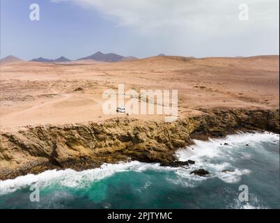 Blick von oben, atemberaubende Aussicht ein Paar mit einem Minibus auf einer Klippe, die vom Meer gebadet wurde. Fuerteventura, Kanarische Inseln. Life-on-the-Road-Konzept Stockfoto