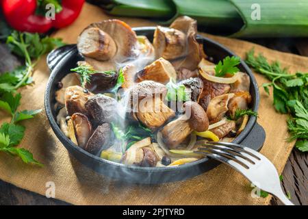 Garen Sie einfach dampfende Steinpilze in der Pfanne auf dem Holztisch. Draufsicht. Stockfoto