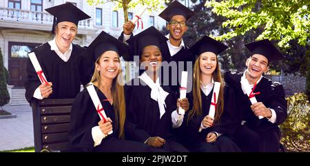 Banner mit Gruppenporträt von freudigen Universitätsabsolventen in Mützen und Kitteln im Freien Stockfoto