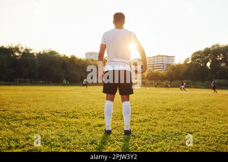 Stehen und den Ball in der Hand halten. Ein junger Fußballspieler trainiert auf dem Sportplatz Stockfoto
