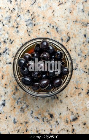 Entsteinte schwarze Oliven in der Schüssel auf dem Küchentisch. Draufsicht. Stockfoto