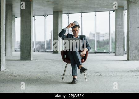 Geschäftsmann im Gebäude. Ein junger Mann in formeller Kleidung arbeitet im Innenbereich an der Baustelle Stockfoto