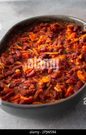 Gesundes Frühstück und Mittagessen, gedünstete rote Bohnen mit Karotten, Zwiebeln und Tomaten, Blick von oben auf eine ovale Keramikrösterei mit gedünsteten Hülsenfrüchten Stockfoto