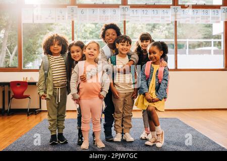 Gruppe von Grundschülern, die im Klassenzimmer zusammenstehen. Multiethnische Kinder, die in die Kamera schauen, mit einem Lächeln im Gesicht. Kinder fühlen sich Stockfoto