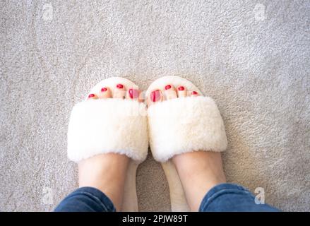 Weiße Hausschuhe, Nahaufnahme der Frauenfüße Tragen Sie weiße Hausschuhe auf dem Teppichhintergrund. Ideal für jeden Gebrauch. Stockfoto