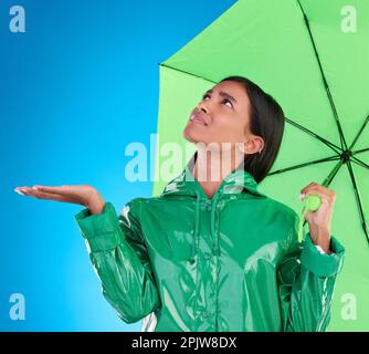 Traurig, aussehend und eine Frau mit Regenschirm, isoliert auf blauem Hintergrund in einem Studio. Verwirrt, Versicherung und ein Mädchen, das auf böse wartet Stockfoto