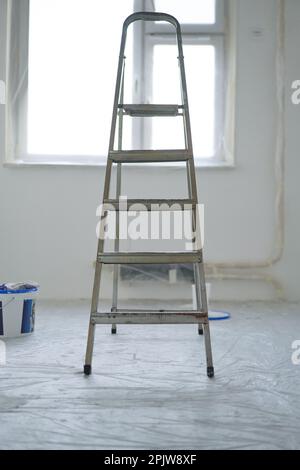 Klappbare Trittleiter aus Metall vor dem Hintergrund von bemalten Wänden im Raum. Konzept der Reparatur- und Veredelungsarbeiten. Stockfoto