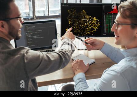 Nahaufnahme zweier Spezialisten für maschinelles Lernen, die vor dem pc über ein neues Projekt im Büro herabsehen und Daten analysieren. Selektiver Fokus auf den Computerbildschirm Stockfoto