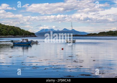 Boote in der Samalaman Bay, mit der Insel Eigg in der Ferne und den Bergen von Rum dahinter, in Glenuig auf der Ardnamurchan-Halbinsel in Lochaber, Schottland Stockfoto