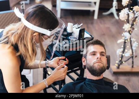 Draufsicht eines Mannes, der auf einem Friseurstuhl neben einer Arbeiterin liegt Stockfoto
