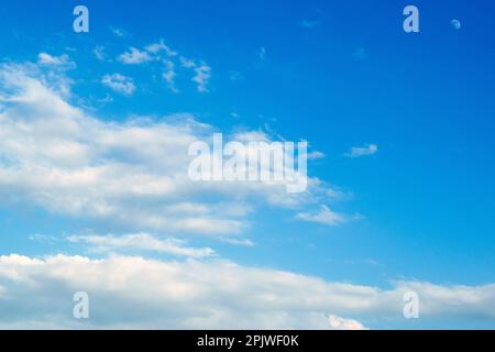 Wunderschöner blauer Himmel mit sichtbarem Mond und ein paar weißen, harmlosen und sommerlichen Wolken. Stockfoto