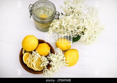 Holzteller mit frischen Zitronen für eine gesunde, erfrischende alkoholfreie Limonade mit Sirup aus Holunderblüten. Stillleben mit frisch geschnittenem Ambuku Stockfoto