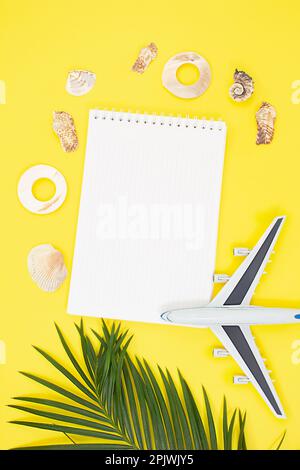 Flugzeug mit Palmenzweigen mit Schalenrahmen um Notizblock auf sommergelbem Hintergrund. Urlaub, Reisekonzept, flache Liegefläche, wenig exotisch Stockfoto