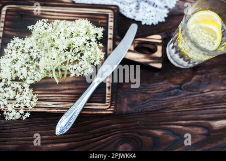 Zerkleinern von Zitrone und schwarzer Holunderbeere auf einem Schneidebrett zur Herstellung eines Kräutergetränks oder eines Medikaments zur Heilung von Sirup aus Holunderblüten zu Hause. Stockfoto