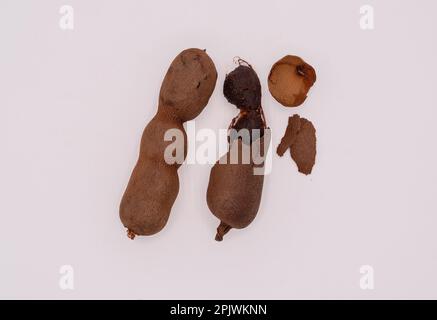 Nahaufnahme von 2 Tamarindenfrüchten, geschält und ungeschält auf isoliertem weißem Hintergrund. Stockfoto