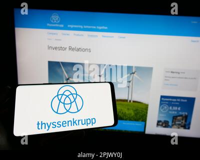 Person, die ein Mobiltelefon mit Logo des deutschen Konglomerats ThyssenKrupp AG auf dem Bildschirm vor der Webseite hält. Konzentrieren Sie sich auf das Display des Telefons. Stockfoto