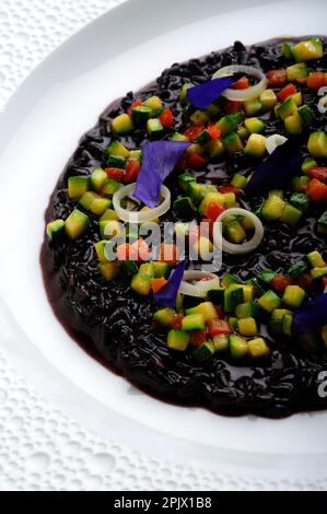 Ein Gericht aus schwarzem Venere Risotto mit Tintenfischtinte und Gemüse der Saison und Kräutern. Stockfoto