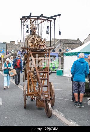 Eine Person auf Stelzen mit einem mobilen Gerät, das einen feuerspeienden Drachen trägt, wie sie etwa 2015 beim Skipton International Puppet Festival zu sehen ist. Stockfoto