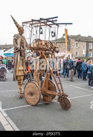 Eine Person auf Stelzen mit einem mobilen Gerät, das einen feuerspeienden Drachen trägt, wie sie etwa 2015 beim Skipton International Puppet Festival zu sehen ist. Stockfoto