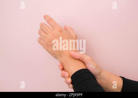 Nahaufnahme der Hand einer Frau mit schmerzhaftem Handgelenk wegen Arthritis oder Karpaltunnelsyndrom (CST), isoliert auf pinkem Hintergrund. Gesundheitskonzept. Stockfoto