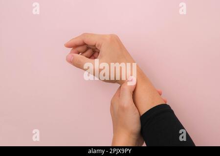 Nahaufnahme der Hand einer Frau mit schmerzhaftem Handgelenk wegen Arthritis oder Karpaltunnelsyndrom (CST), isoliert auf pinkem Hintergrund. Gesundheitskonzept. Stockfoto