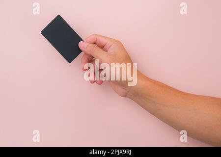 Nahaufnahme der Hand einer Frau mit schwarzer Karte isoliert auf pinkfarbenem Hintergrund. Stockfoto